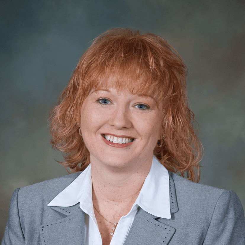 Smiling woman with red hair wearing a gray blazer.
