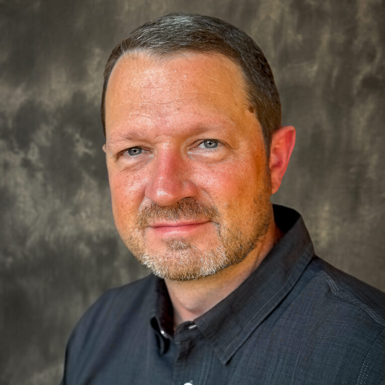 A middle-aged man with short hair and a beard, wearing a black shirt, smiles at the camera.