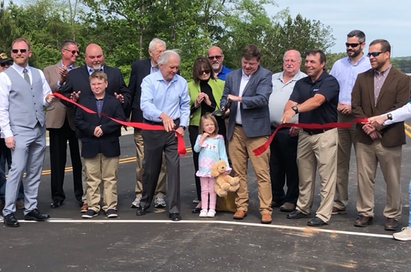 Group of people cutting a red ribbon on a road.