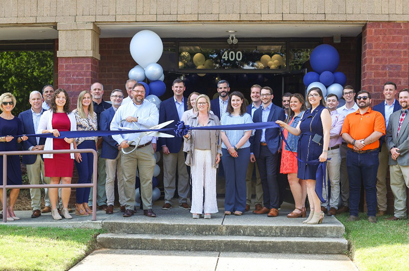 Group of people cutting a blue ribbon in front of a building.